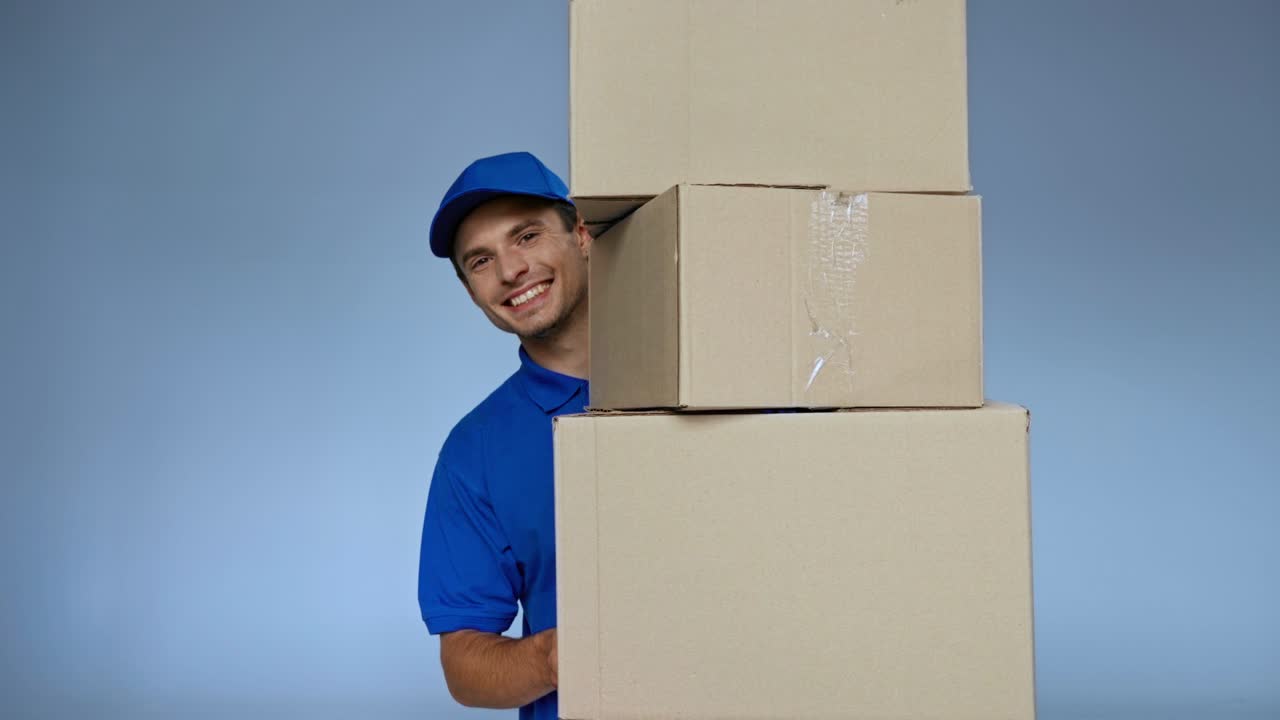 hombre de entrega feliz con gorra sosteniendo cajas de cartón en gris