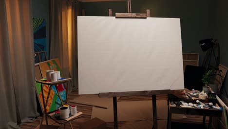 un espacio de trabajo, un estudio de un pintor, un artista con un gran caballete con un lienzo en el medio de la habitación. alrededor del lienzo esparcidas pinturas, pinceles, cajas de cartón, un lío