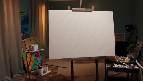 a workspace, a studio of a painter, an artist with a large easel with a canvas in the middle of the room. around the canvas scattered paints, brushes, cardboard boxes, a mess