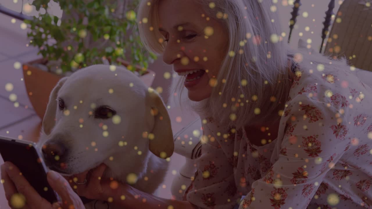 Donna anziana che avvicina il telefono al cane, accarezzandolo mentre scorre per condividere tecnologia, con sovrapposizione di bokeh dorato