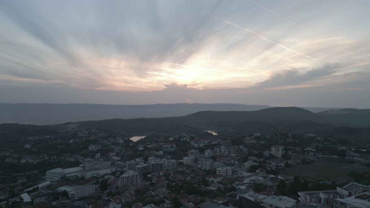 droneshot desde arriba kruje albania volando sobre la ciudad en el acantilado en un día nublado con nubes contra las montañas durante el atardecer