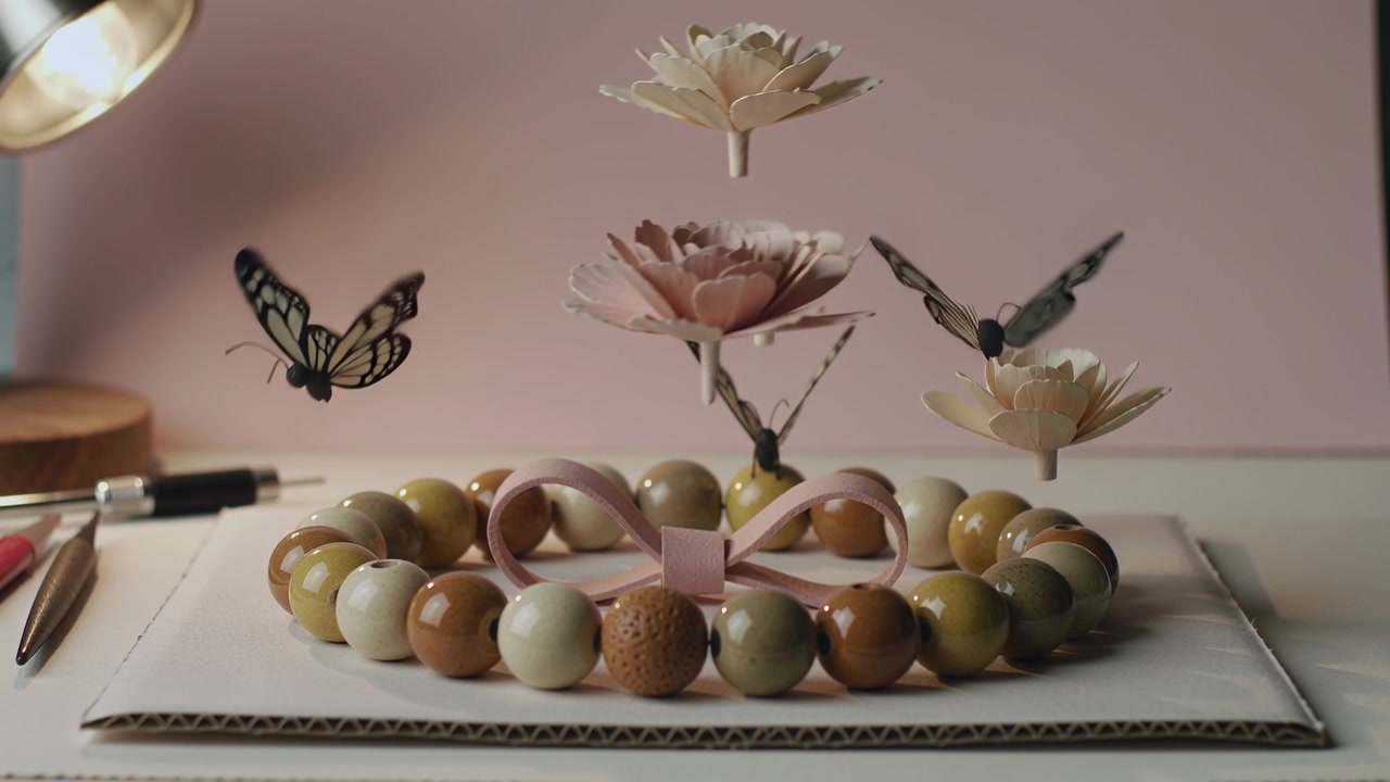 Playback starting, butterfly cutouts fluttering near bead ring flowers on table showing pink ribbon