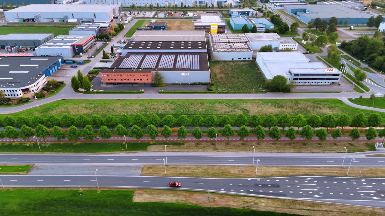 Warehouses by the highway. An aerial view of a bustling industrial area featuring various warehouses, greenery, and a nearby highway
