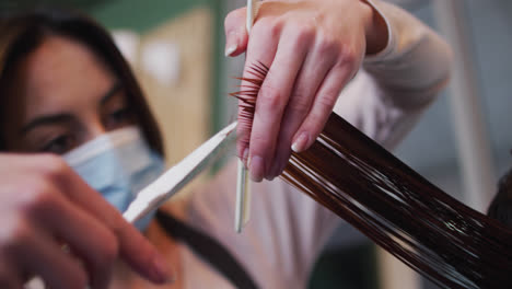 Female-hairdresser-wearing-face-mask-cutting-hair-of-female-customer-at-hair-salon