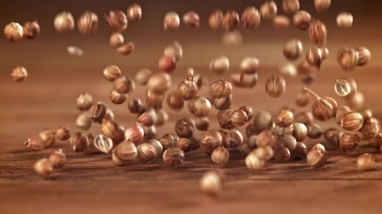 Close-up of Coriander Seeds Falling onto Wooden Surface in Slow Motion