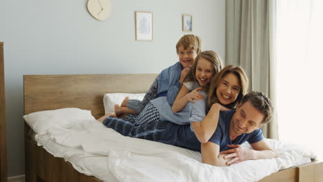 alegres padres e hijos acostados uno en la parte posterior del otro en la cama y sonriendo a la cámara