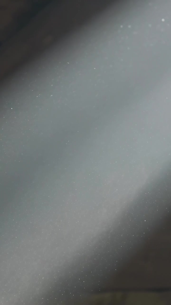 Vertical video: Moving grey blur passing across lens after hand motion revealing rafters and dust