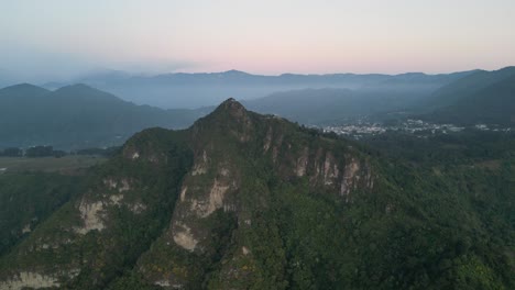 Drone-view-in-Guatemala-flying-in-front-of-a-green-mountain-surrounded-by-volcanos-on-a-cloudy-day-in-Atitlan