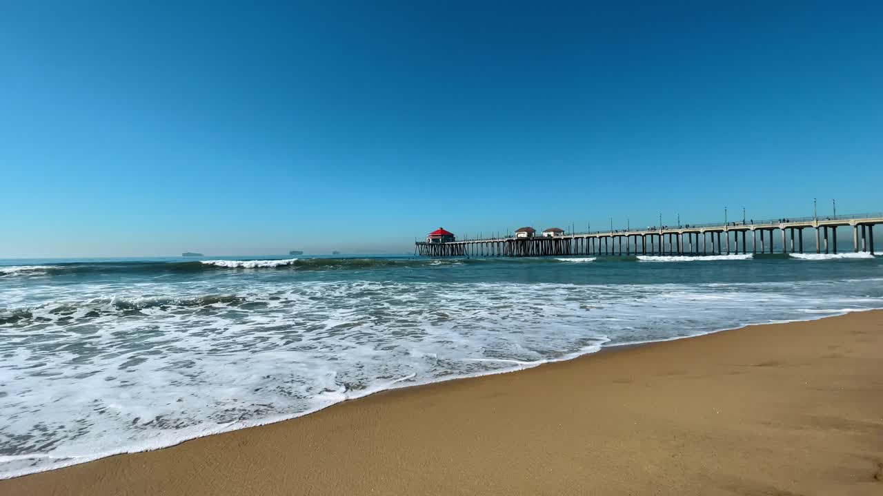 Il molo di Huntington Beach che si estende nell'Oceano Pacifico. Ampia visuale di un molo in legno con un edificio dal tetto rosso sopra le onde dell'oceano in California, USA.