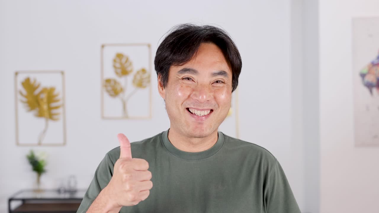 A man smiles and gives a thumbs up in a well-lit room with decorative wall art