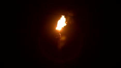 una toma nocturna de una antorcha de gas en llamas de la producción petroquímica en completa oscuridad. combustión de petróleo de baja clave y contaminación ambiental. concepto de problemas ecológicos
