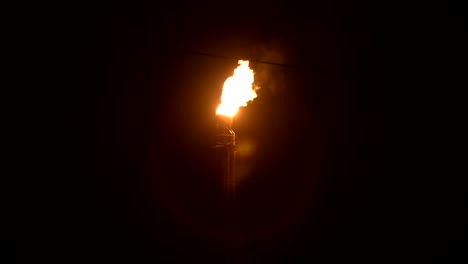 a night shot of a flaming gas torch of petrochemical production in complete darkness. low key oil combustion and environmental pollution. ecology problems concept