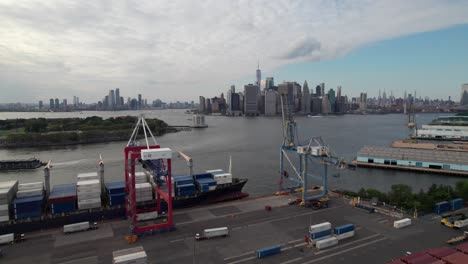 gran barco de contenedores siendo cargado con el horizonte de manhattan en el fondo, 4k aérea