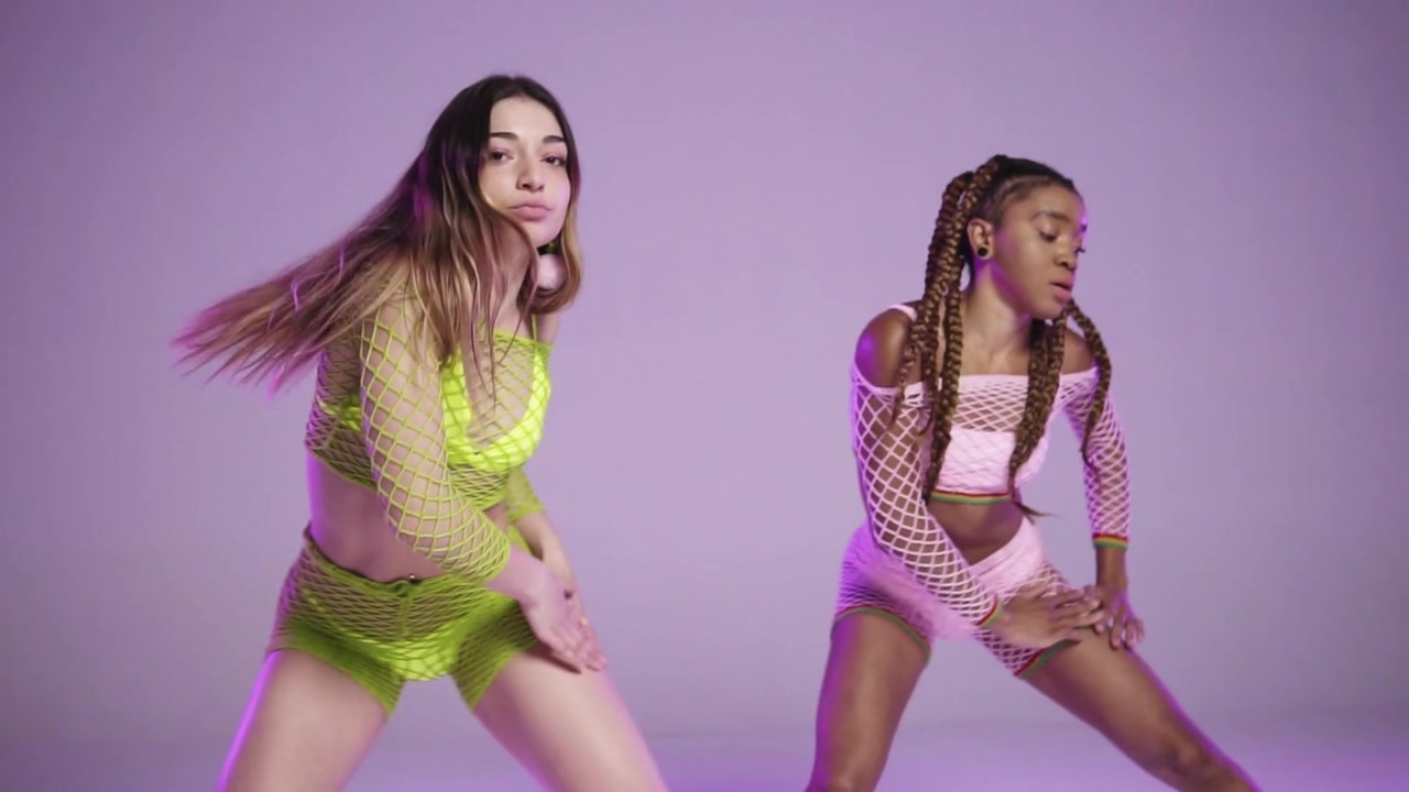 Tre ballerine eseguono lo stesso movimento con abiti vivaci e colorati in un ambiente da studio, a velocità rallentata.