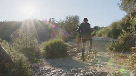hiker traversing leashed trail with small dog, rocky terrain backlit by golden morning sunlight in scenic wilderness setting