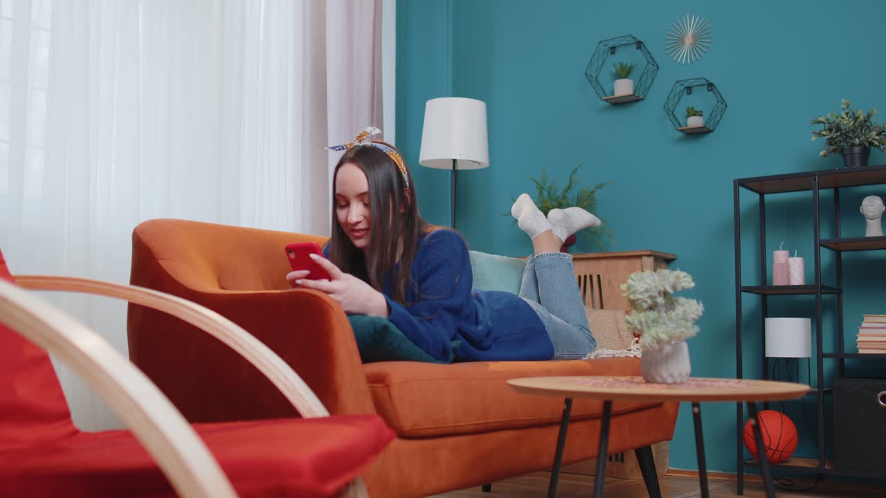 Cheerful young woman lying on sofa using mobile phone share messages on social media application