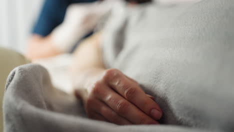 female client rests peacefully on spa bed, hand relaxed atop soft gray blanket, during calming skincare treatment in tranquil wellness center atmosphere under natural light