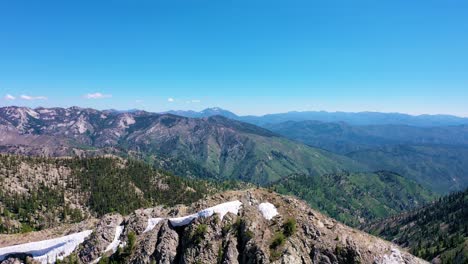 Drone-aerial-shot-pulls-out-from-over-a-snowy-mountain-range-view-revealing-a-beautiful-forest-and-a-backcountry-lake