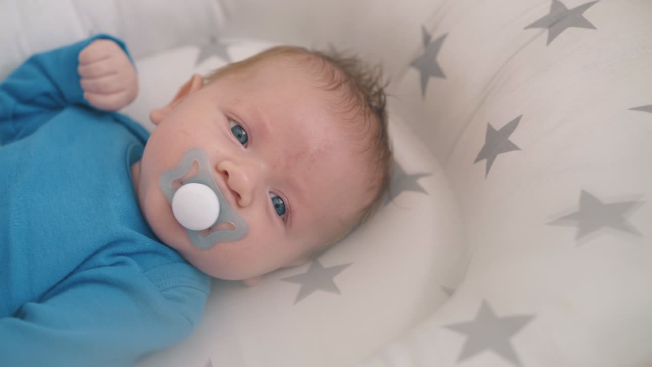little child with dummy kicks legs in cocoon in wooden cot