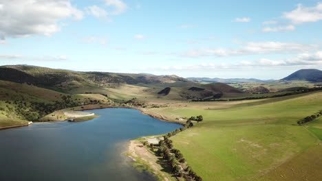 slow drone pan over rural dam with dirt road winding through hillside in tasmania, australia