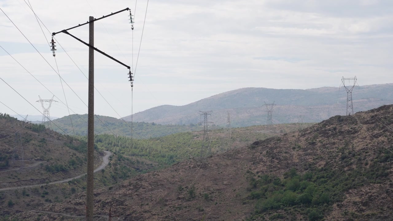 Power Lines Cross Rugged Mountain Valley Under Hazy Skies