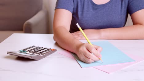 woman is using a calculator to calculate her monthly expenses and write down her monthly accounting records at home