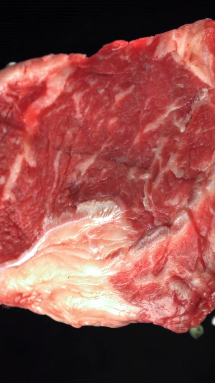 塩と調味料が振りかけられる生牛肉ステーキのクローズアップ