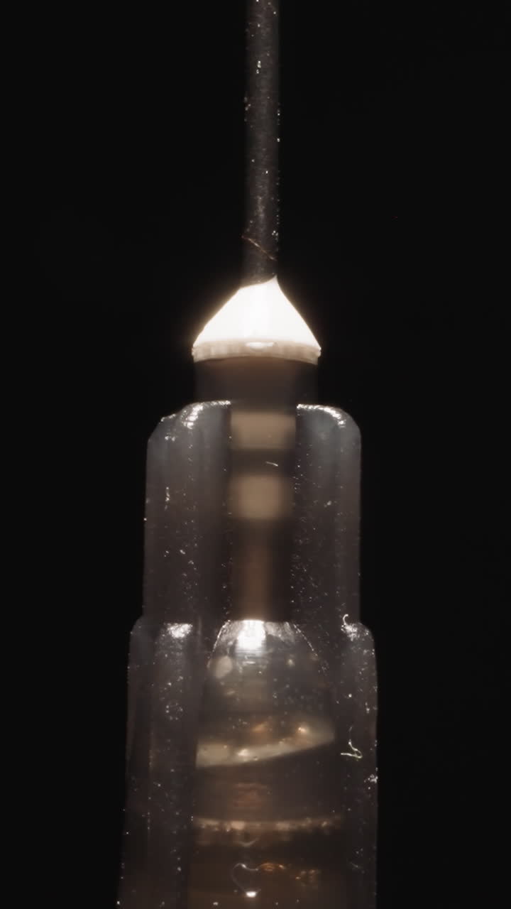Old syringe with rusty needle rotates at bright studio light on black background. Small plastic tube used for injecting and withdrawing liquids macro