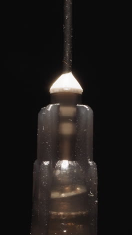 old syringe with rusty needle rotates at bright studio light on black background. small plastic tube used for injecting and withdrawing liquids macro