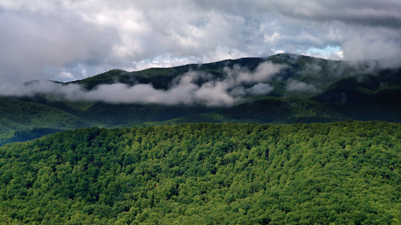 Overhead cinematic shot of cloud systems pressing into misty mountain terrain