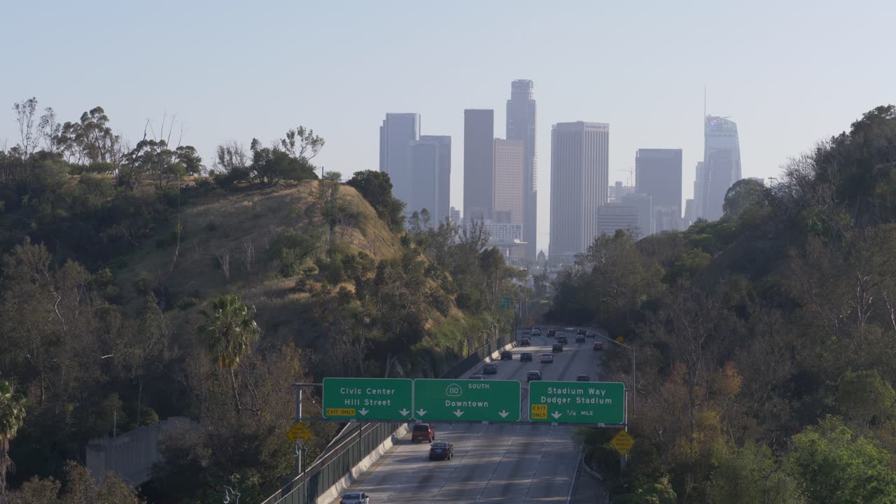 Drone footage of Downtown Los Angeles entrance with view of Stadium Way and Dodger Stadium overpass. The city skyline stands in the background under clear skies