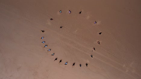 topdown ascending shot of surf lesson, people in a circle warm up on sand, orbiting motion