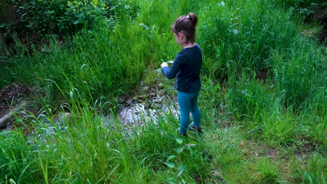 Little-girl-playing-with-a-knife-in-nature,-cutting-grass-into-a-small-stream-in-the-woods,-outdoor-survival-knife,-tool-used-by-a-child