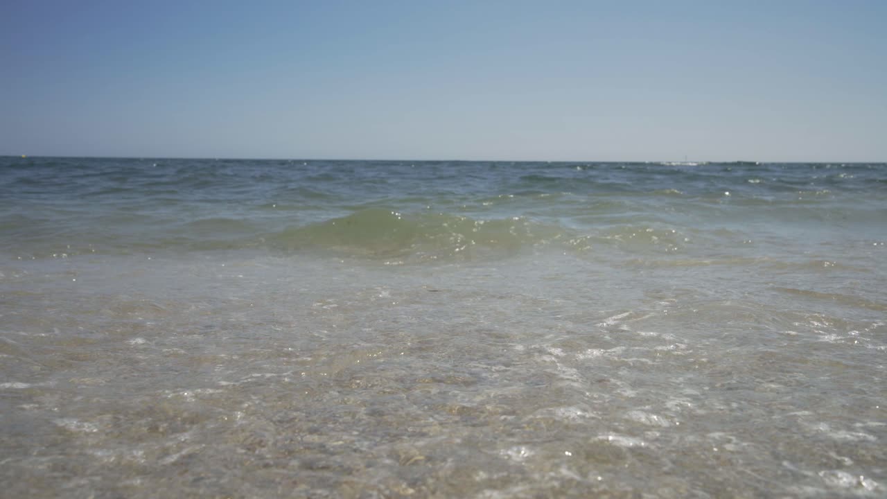 Looking out to sea on a beautiful sunny day as the waves gently wash in along the shore of the fine gravelly beach.