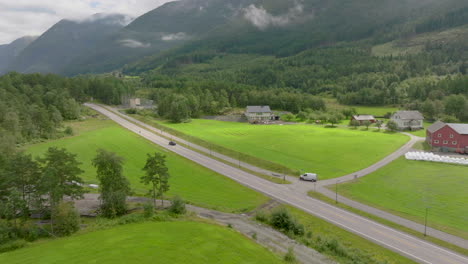 Following-car-travelling-on-road-through-green-farmland-at-base-of-mountain-range