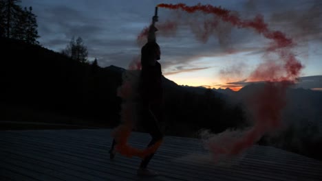 slow motion: silhouette of a young woman dancing on a plattform at dusk holding purple smoke bengala flare