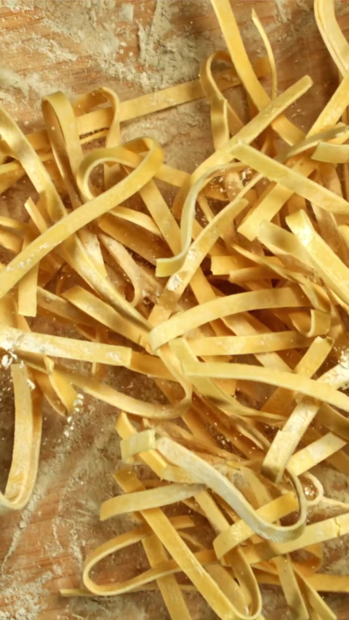 Tagliatelle fresche che cadono su un tagliere di legno infarinato