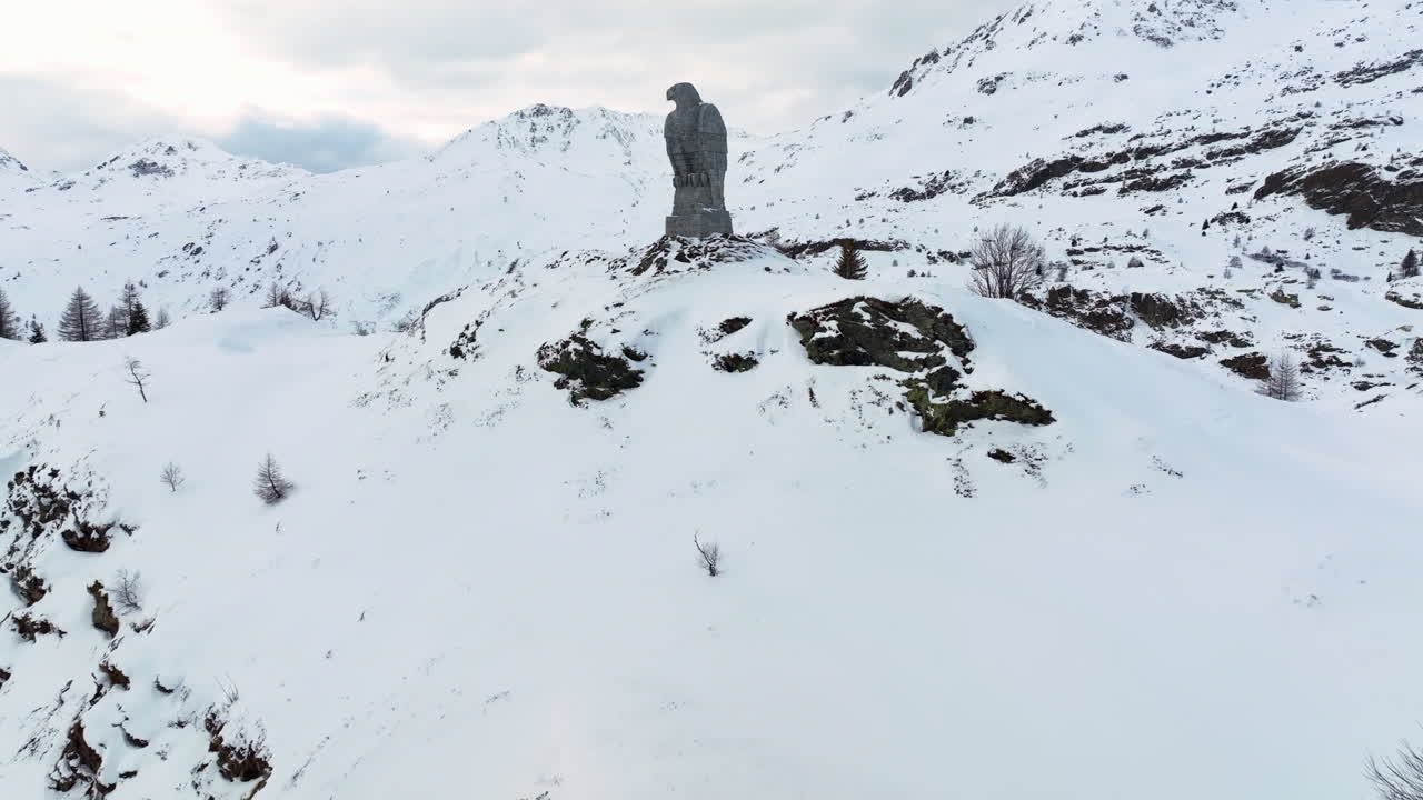 simplon에서 돌의 독수리 조각은 눈으로 덮인 높은 스위스 알프스를 배경으로 통과합니다.