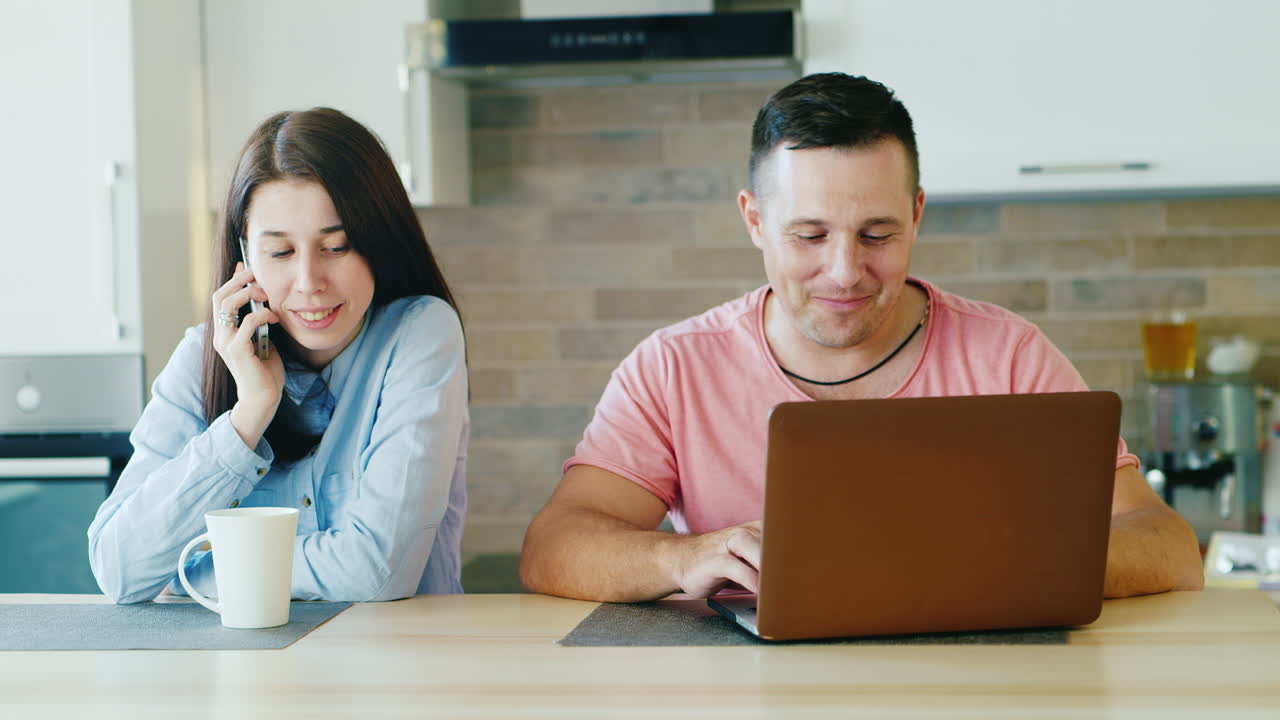 familia joven en la cocina su marido trabaja con una mujer portátil hablando por teléfono