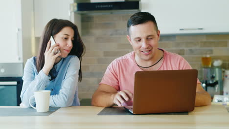 young family in the kitchen her husband works with a laptop woman talking on the phone