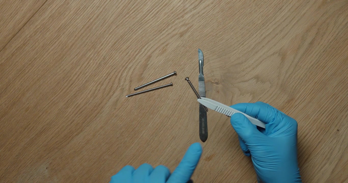 Uma pessoa manuseia um bisturi cirúrgico apenas com pinças, usando luvas de proteção, demonstrando procedimentos de manuseio seguro. Conceito de segurança no trabalho, prevenção de contaminação, trabalho de precisão