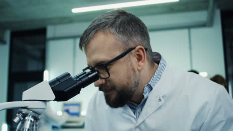 Retrato-Del-Hombre,-Investigador-Médico,-Mirando-En-El-Microscopio-Mientras-Hace-Un-Análisis-Y-Los-Escribe-En-La-Computadora-Portátil-Del-Laboratorio