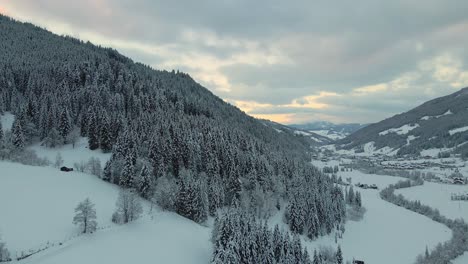 Aerial-shot-of-a-snow-covered-mountain-town,-winding-road-through-the-valley