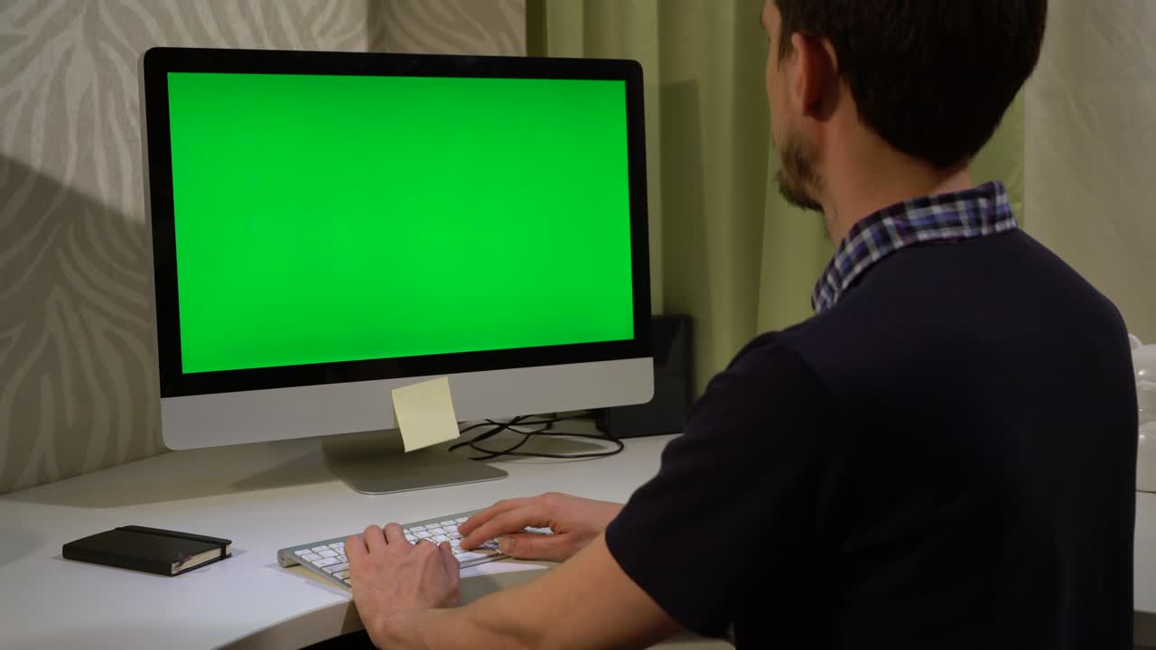 un joven está escribiendo en un teclado frente a un monitor con una pantalla verde