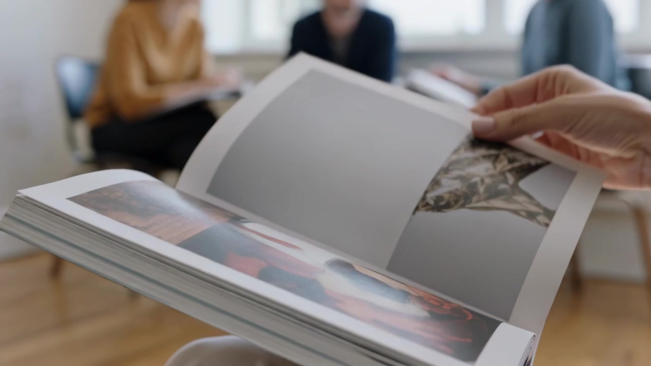 Des mains feuilletant des pages, accompagnant une discussion de groupe en réunion, tenant un livre brillant, des collègues en pulls.