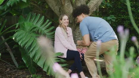 Happy-diverse-couple-having-picnic-in-garden-on-sunny-day