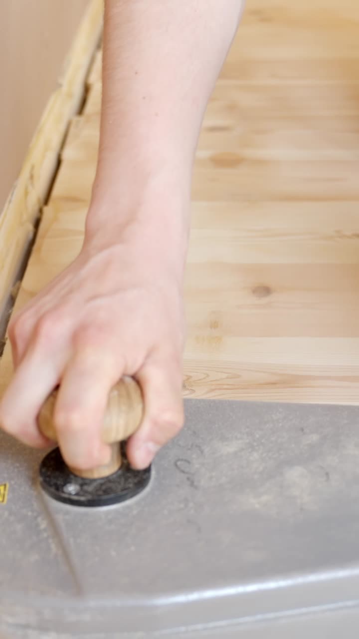 Hand holding control knob of floor sander during wooden floor restoration, vertical