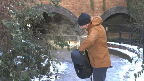 hombre abrigado poniendo una bolsa de transporte de drones en una mochila junto a la arcada del lago brooklands de nieve