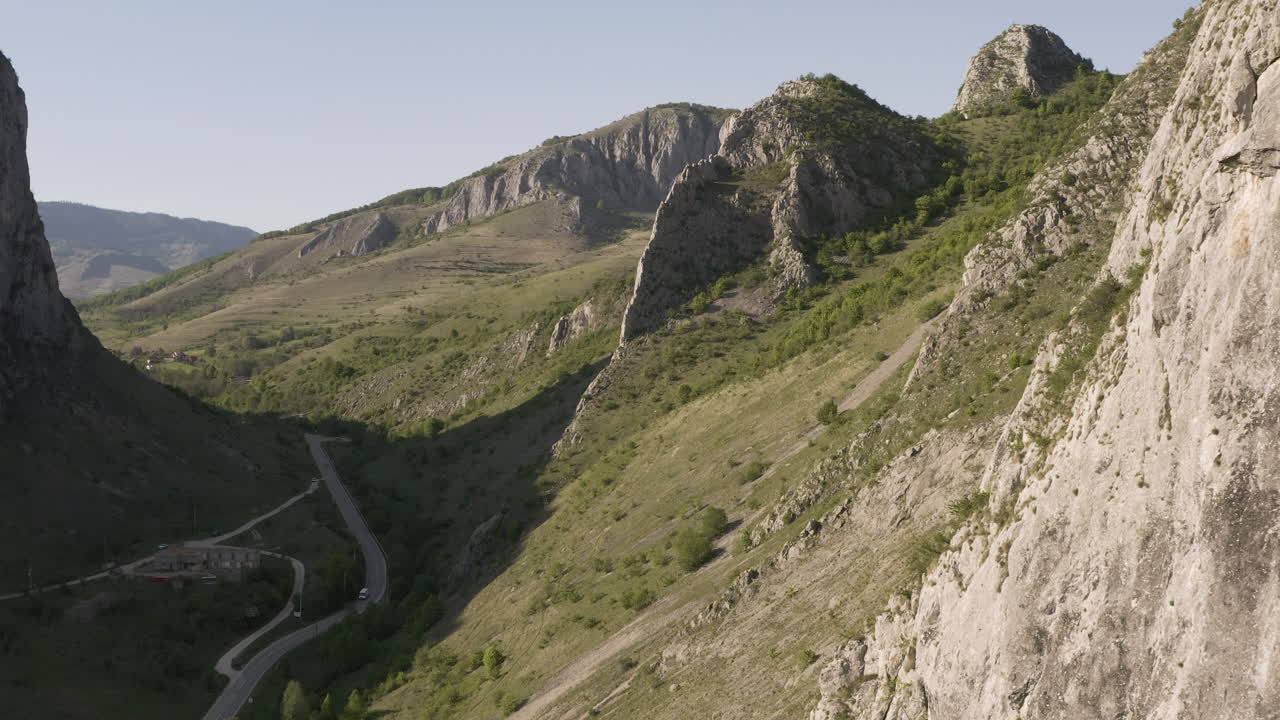 Ripido e roccioso versante montano nell'area ricreativa di Cheile Valisoarei in Romania, vista aerea sopra un'auto che percorre una strada tortuosa nella valle.
