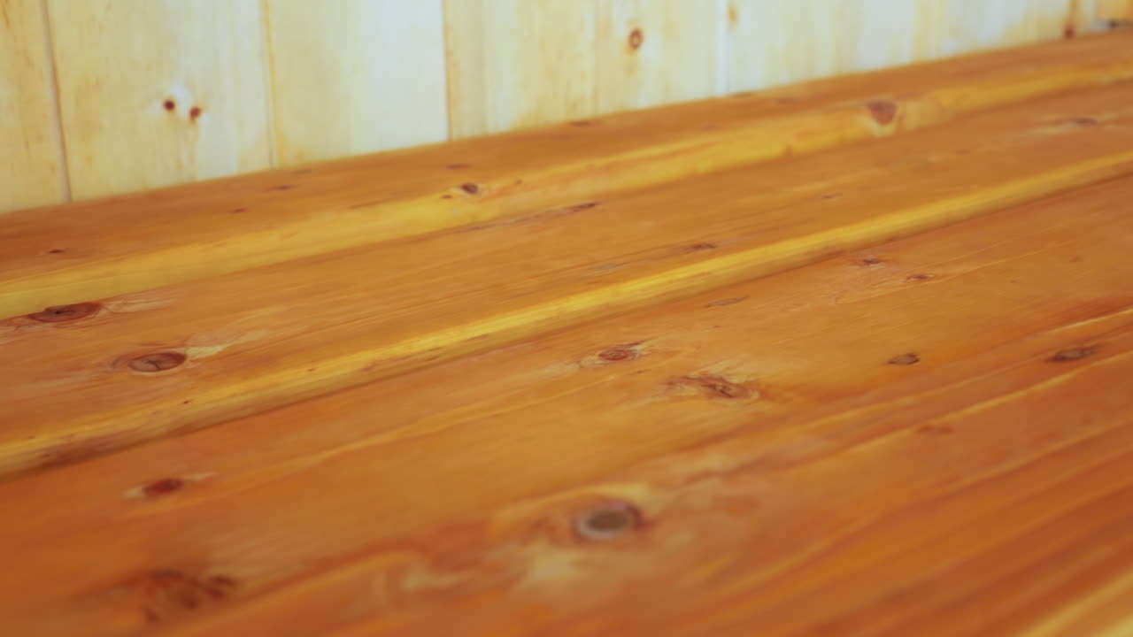 Close up of smooth wooden table featuring warm honey-toned planks and visible natural wood grain and knots, showcasing handcrafted surface detail and rustic indoor ambiance in softly lit setting